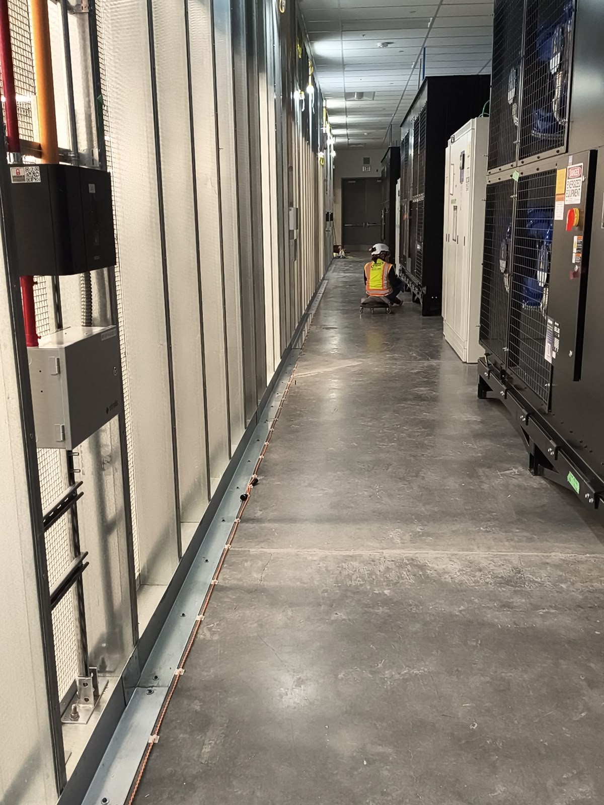 NOVA technician in safety gear cleaning the floor of an equipment aisle inside an operating data center