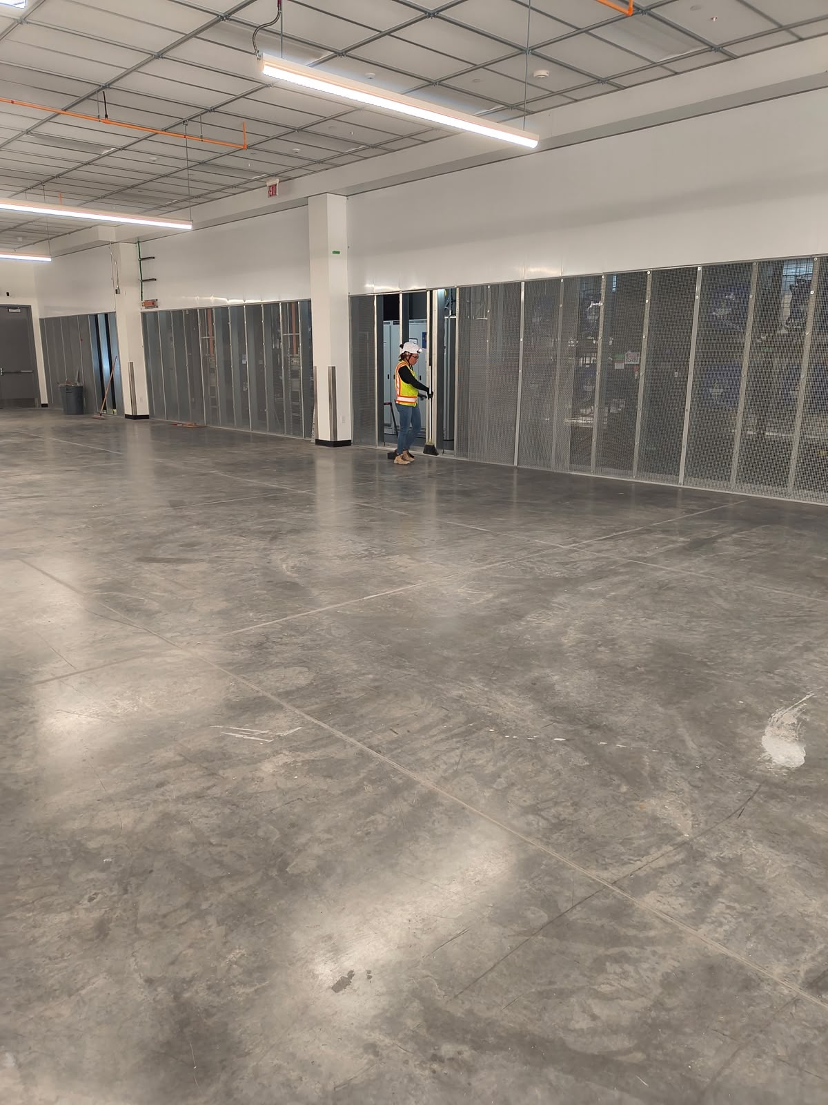 Technician cleaning the floor of a nearly completed data center room with electrical enclosures along the wall